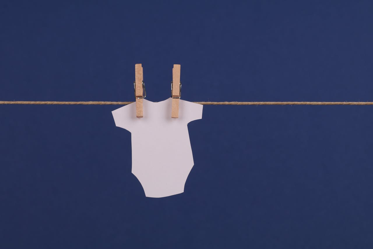 Minimalist baby onesie cutout hanging with clothespins on a blue background, perfect for design mockups.